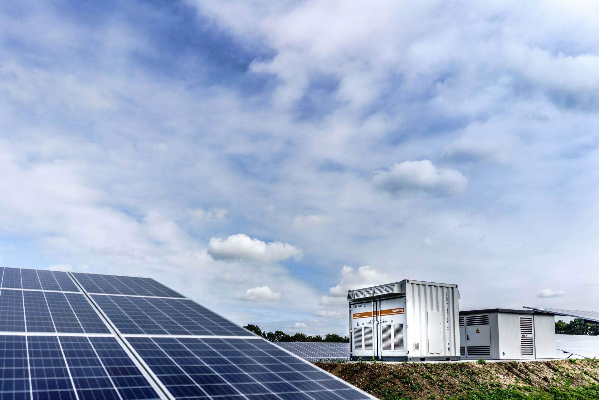 Panneaux solaires dans un champ avec bâtiment de stockage sous un ciel nuageux.