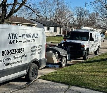 Two plumbing service vans with a trailer parked in a residential driveway.
