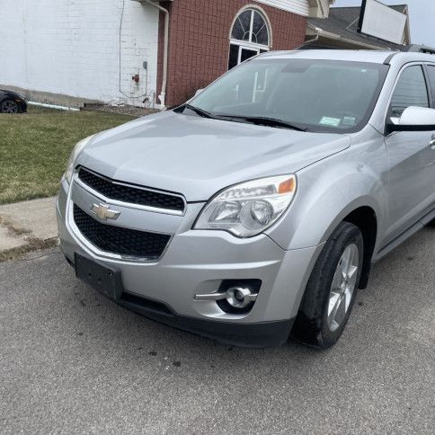 A silver chevrolet equinox is parked on the side of the road in front of a brick building.