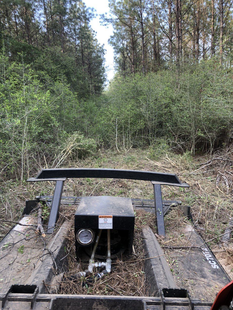 A tractor is driving down a dirt road in the woods.