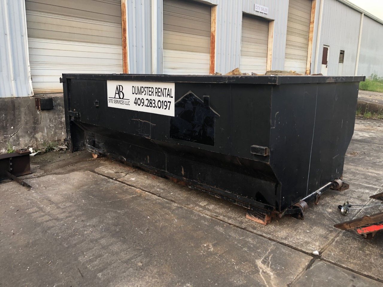 A large black dumpster is parked in front of a building.