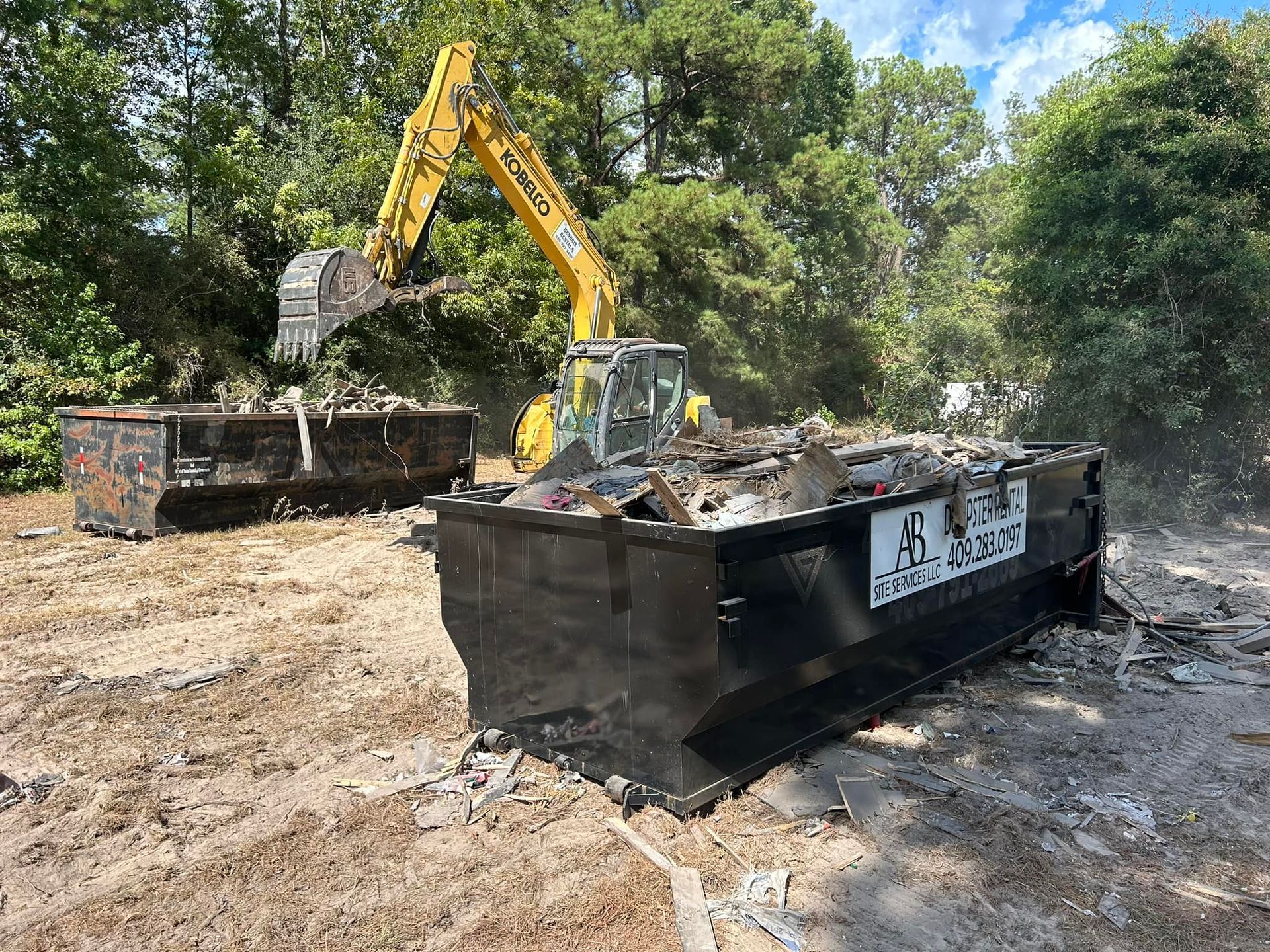 A large dumpster is being demolished by a yellow excavator.