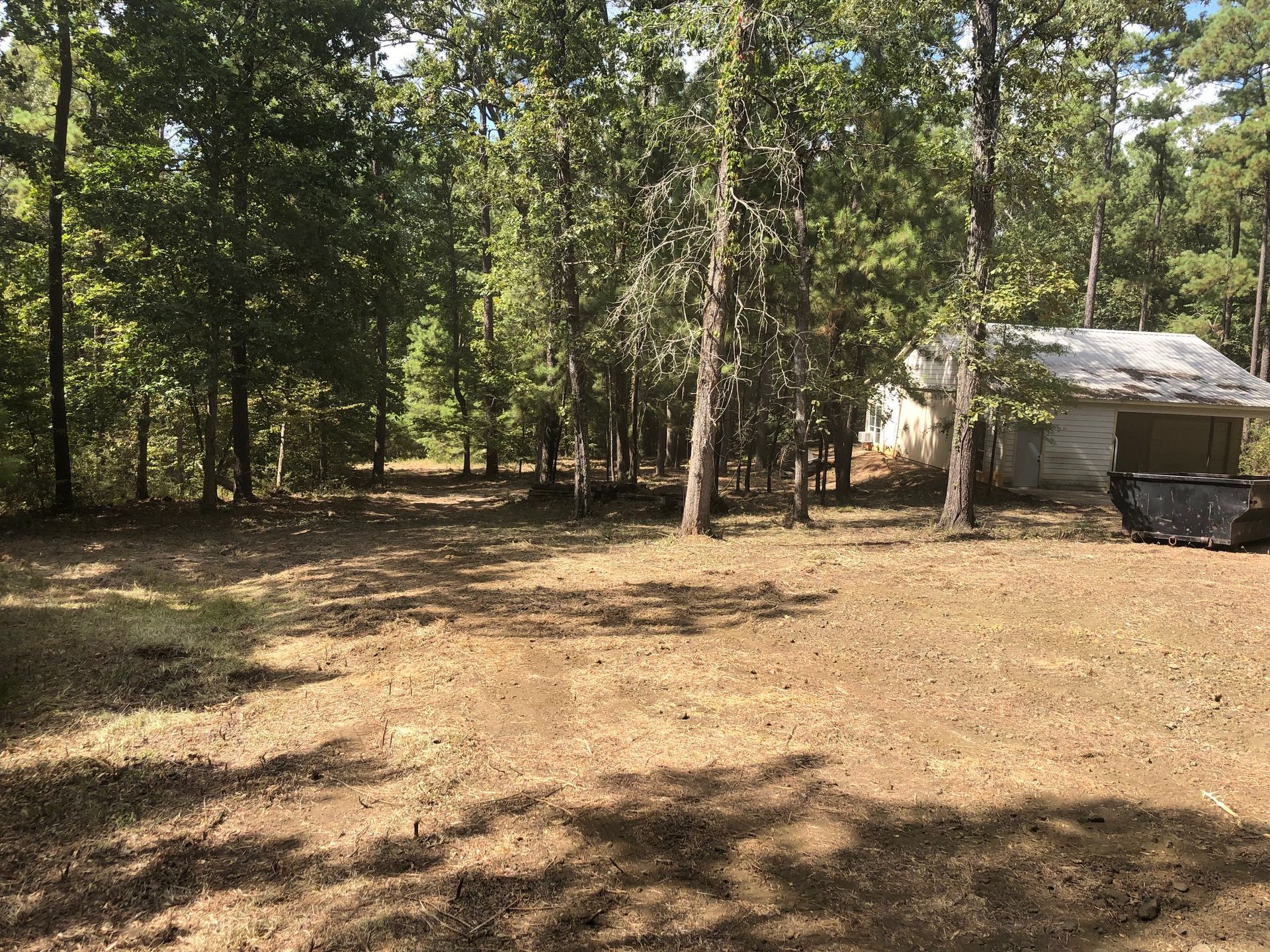 A dirt field with trees and a garage in the background.