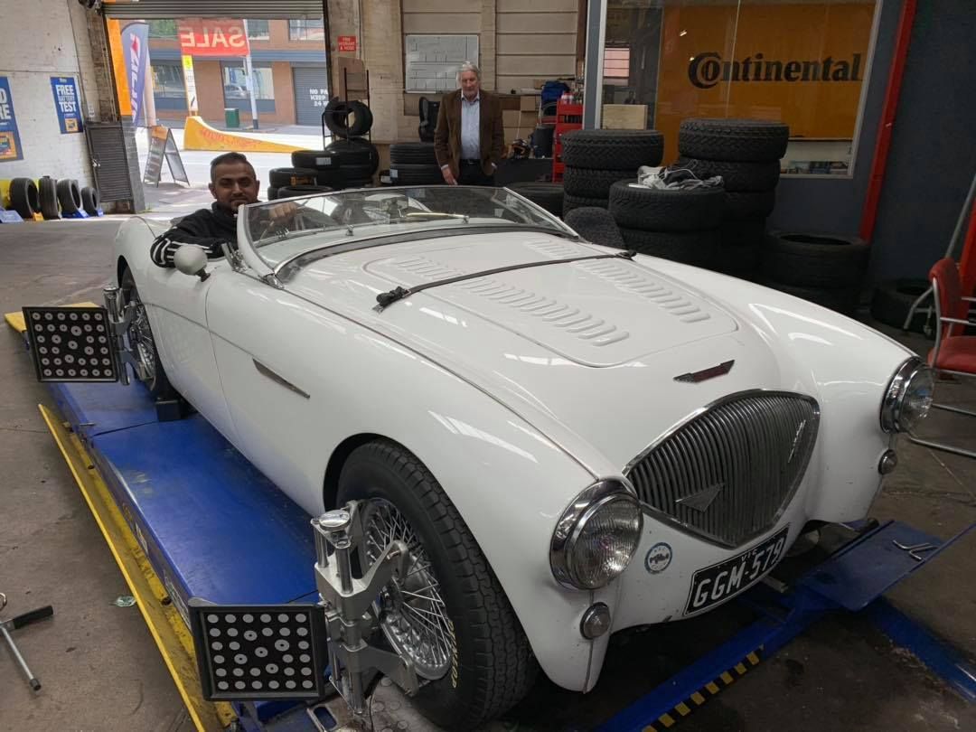 Man in a white classic car on alignment equipment inside a garage.