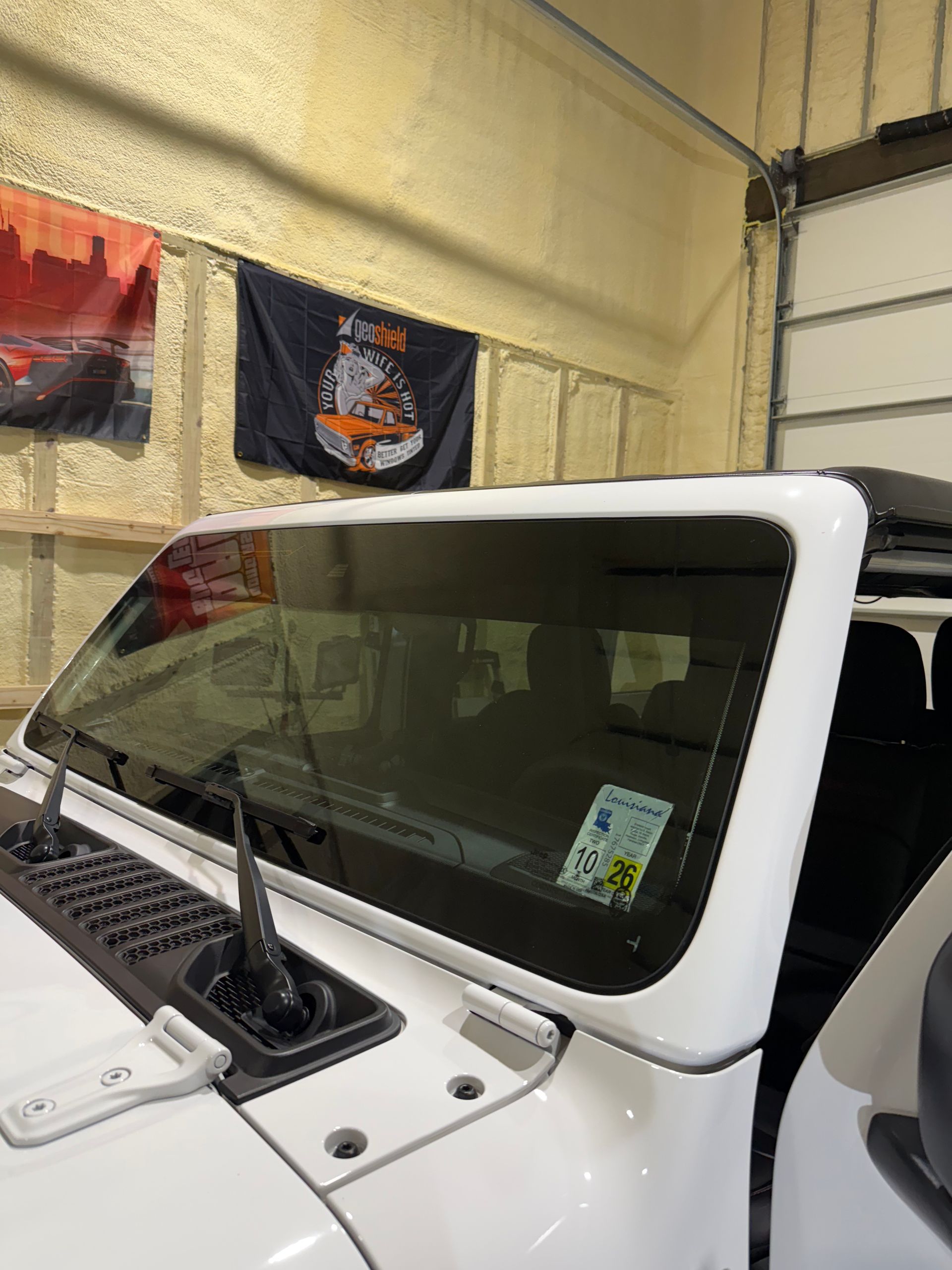 A white jeep is parked in a garage with flags hanging on the wall.
