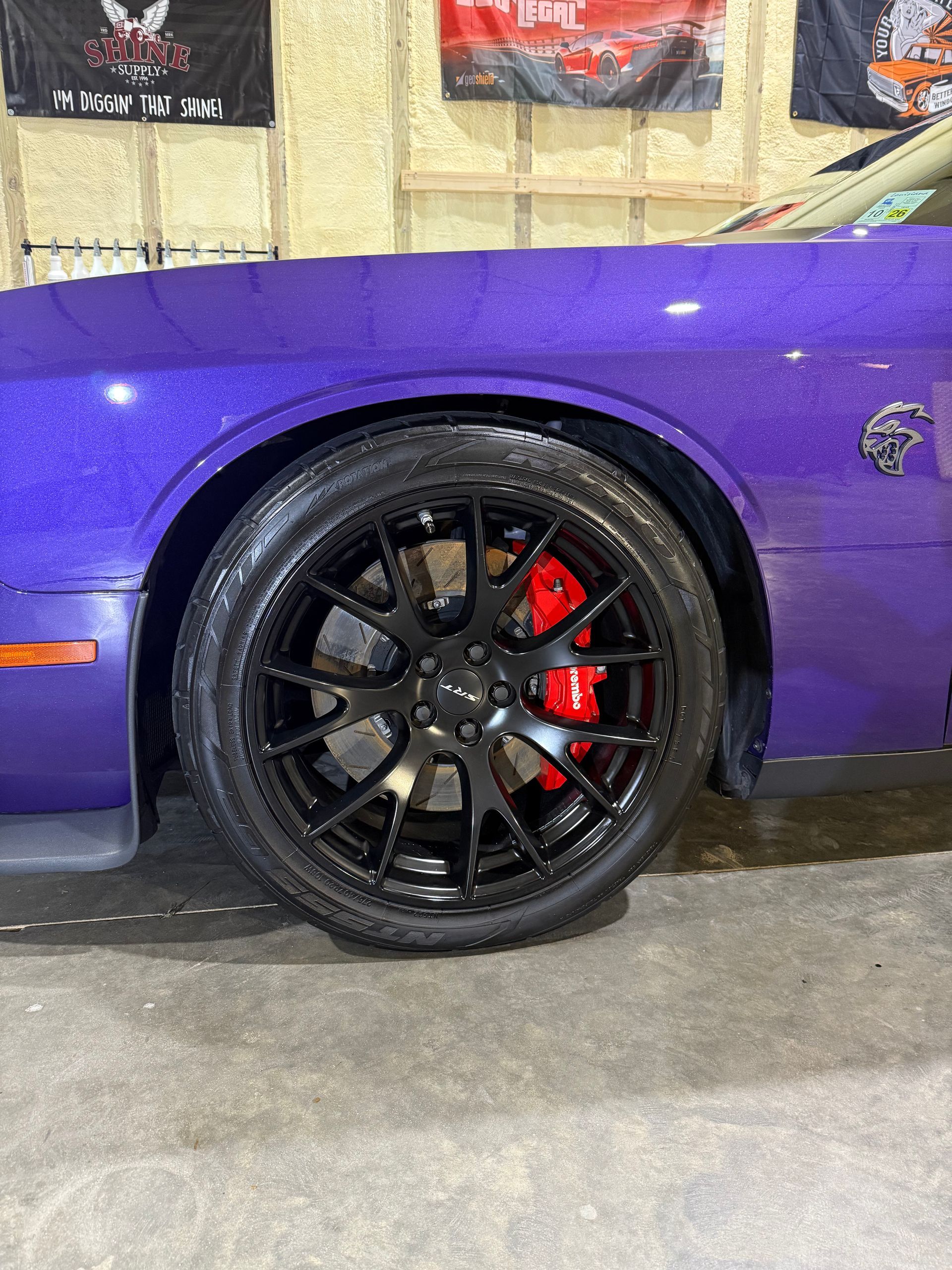 A purple dodge challenger with black wheels and red brake calipers is parked in a garage.
