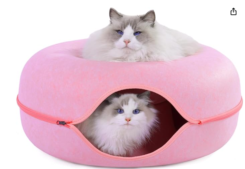 two cats are laying in a pink donut shaped cat bed .