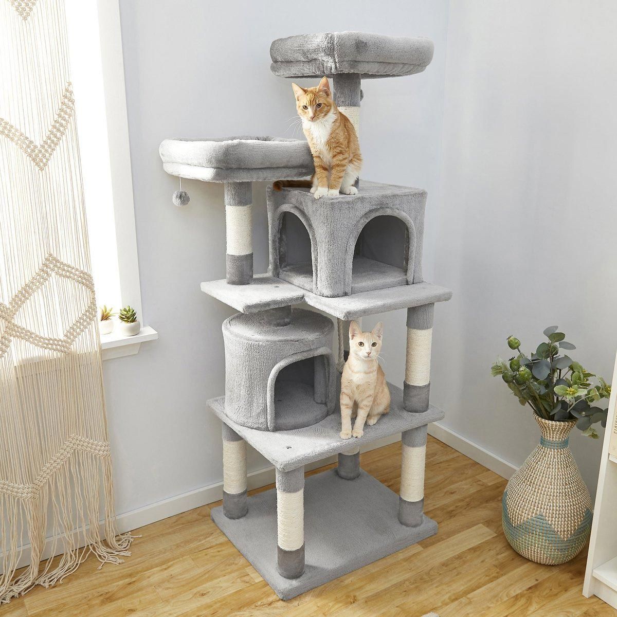 two cats are sitting on top of a cat tree in a living room .