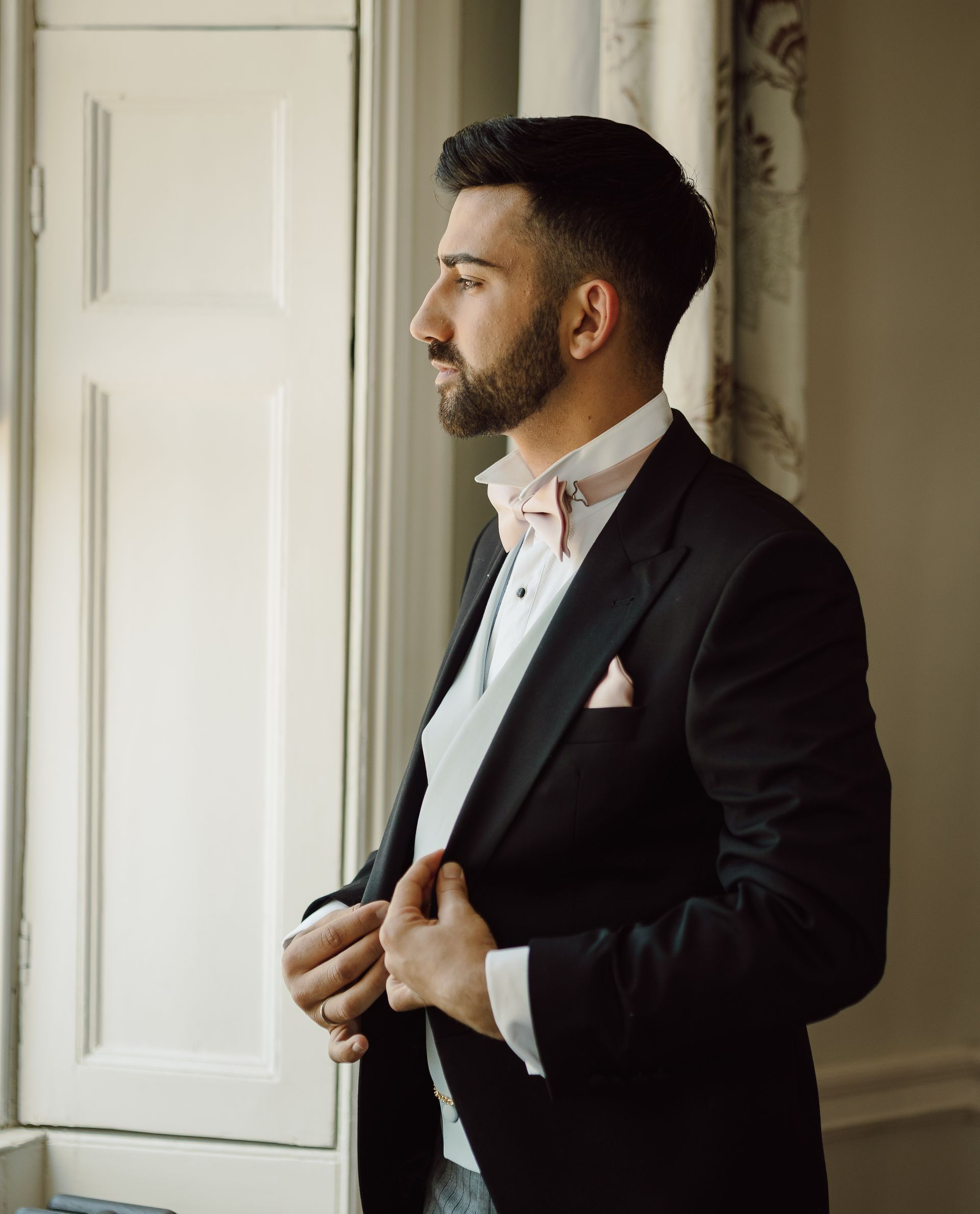 a man in a suit and bow tie is standing in front of a window .