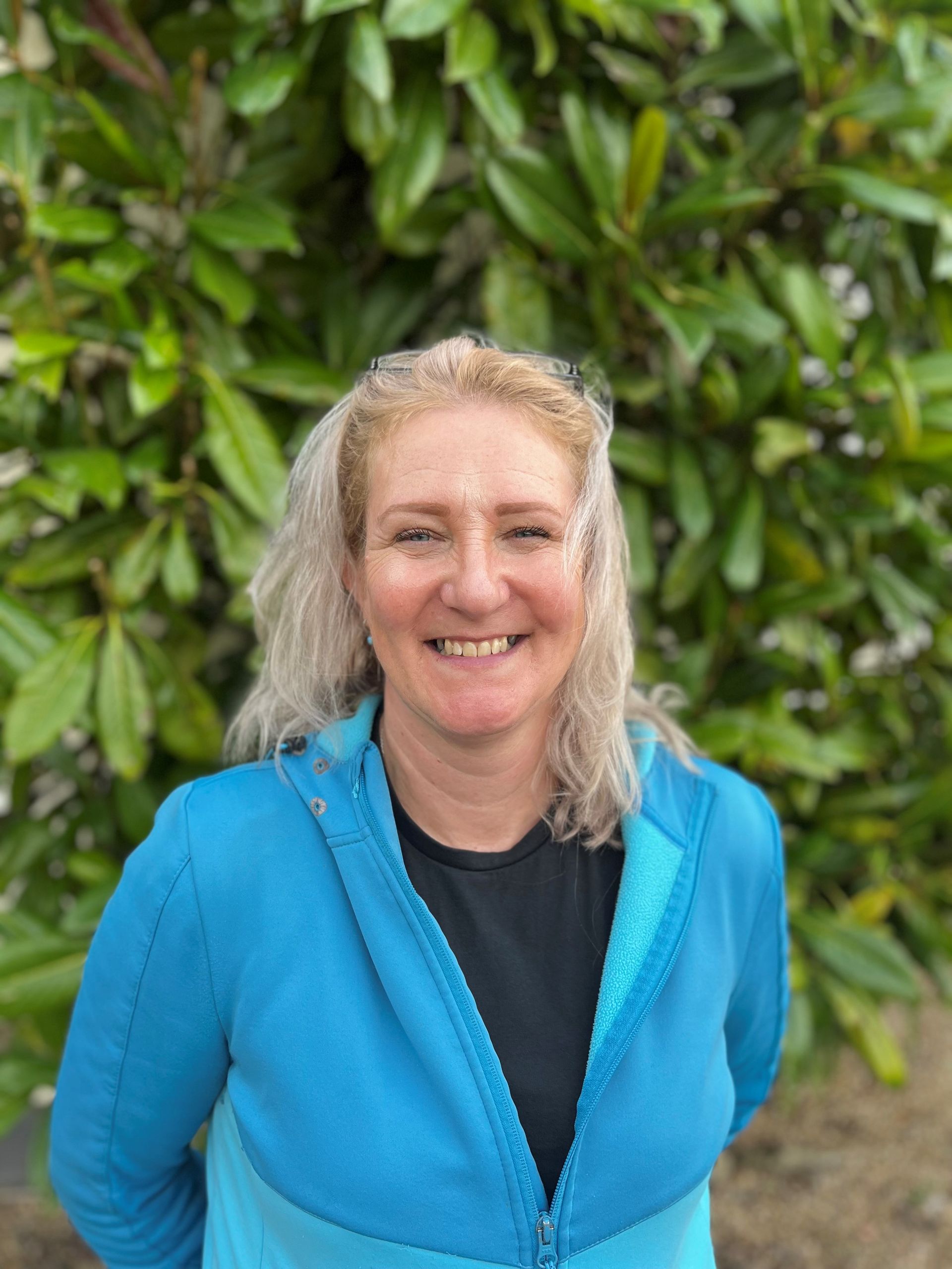 a woman in a blue jacket is smiling in front of a tree .