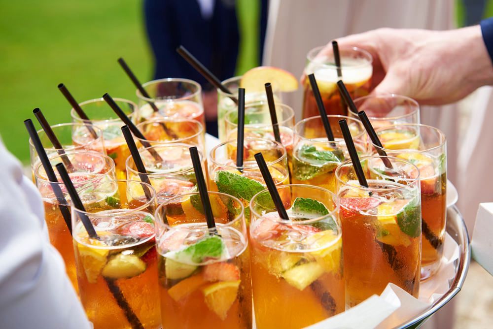 a person is holding a tray of fruity drinks with straws .