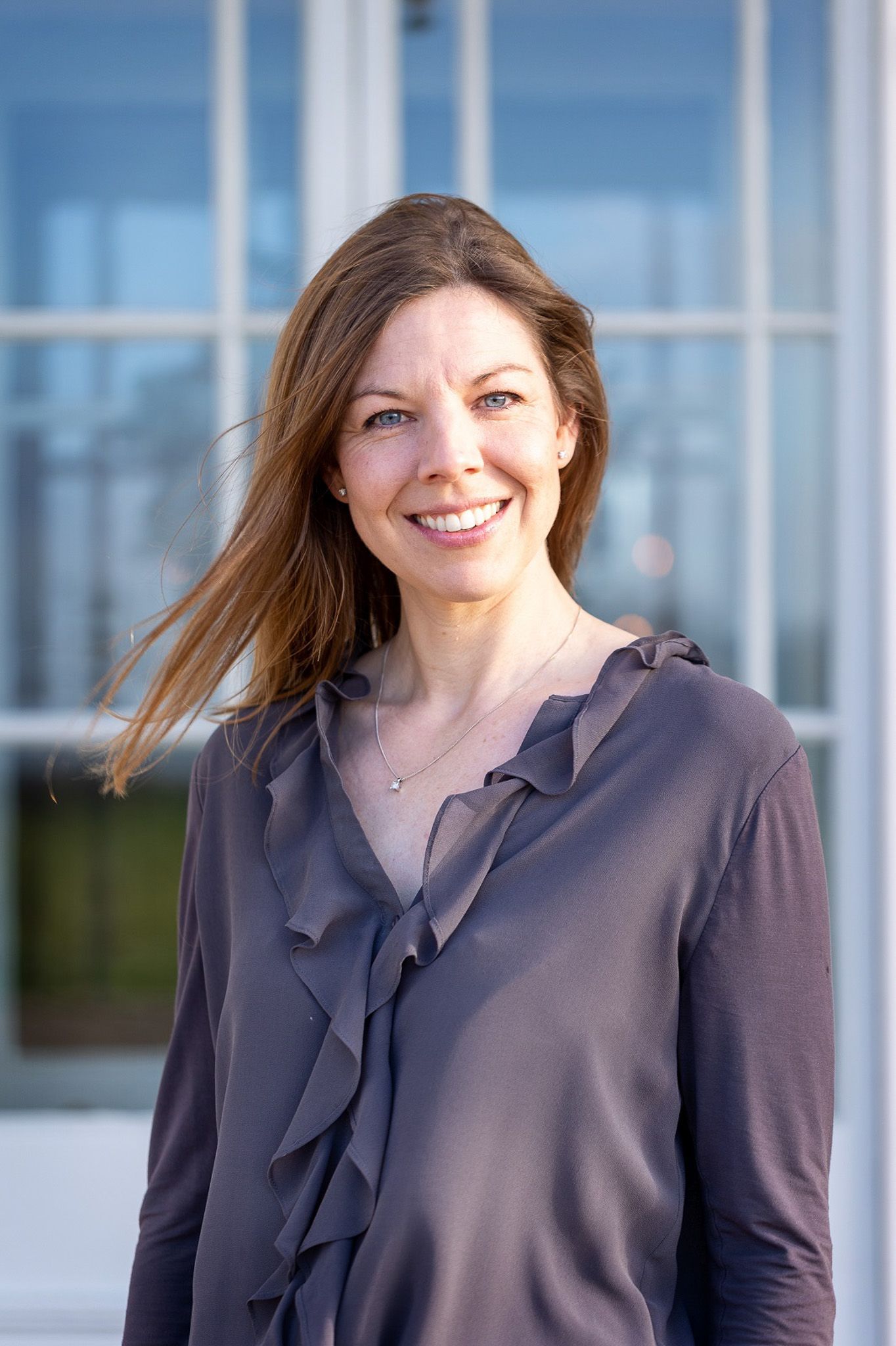 a woman in a ruffled shirt is smiling in front of a window .
