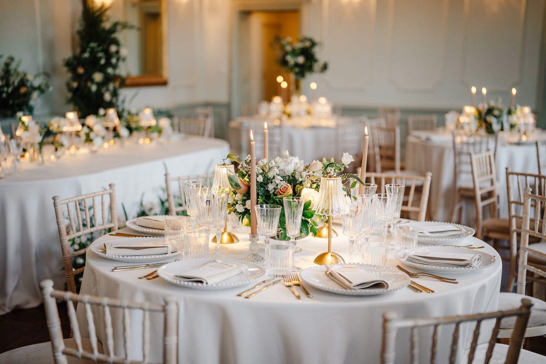 Elegant wedding reception with round tables, white tablecloths, floral centerpieces, and candles.