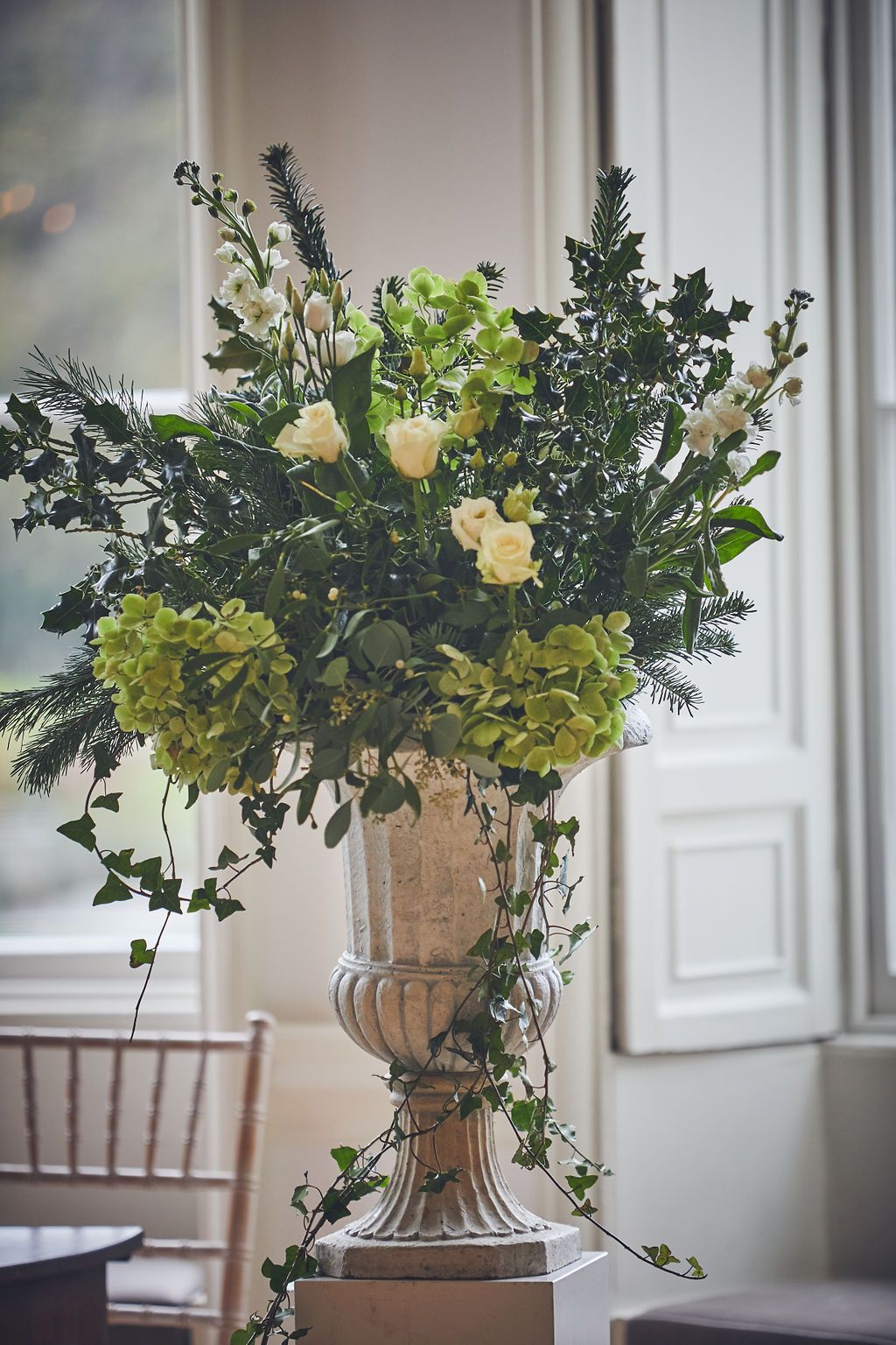a large vase filled with green and white flowers is sitting in front of a window.