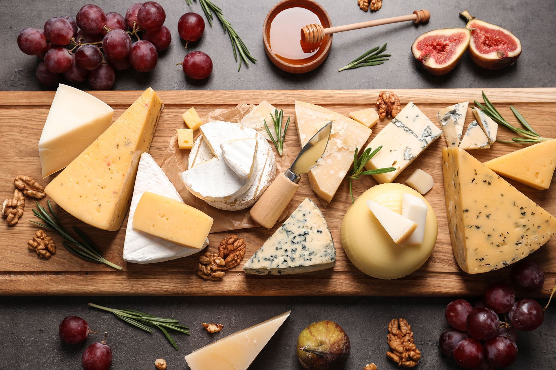 a wooden cutting board topped with different types of cheese , grapes , figs and walnuts .