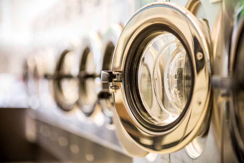 A woman is standing in front of a washing machine in a laundromat.