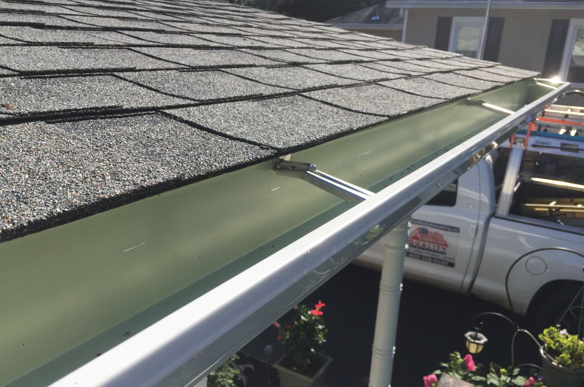 Green gutter installed on a shingled roof, with a white truck visible in the background.