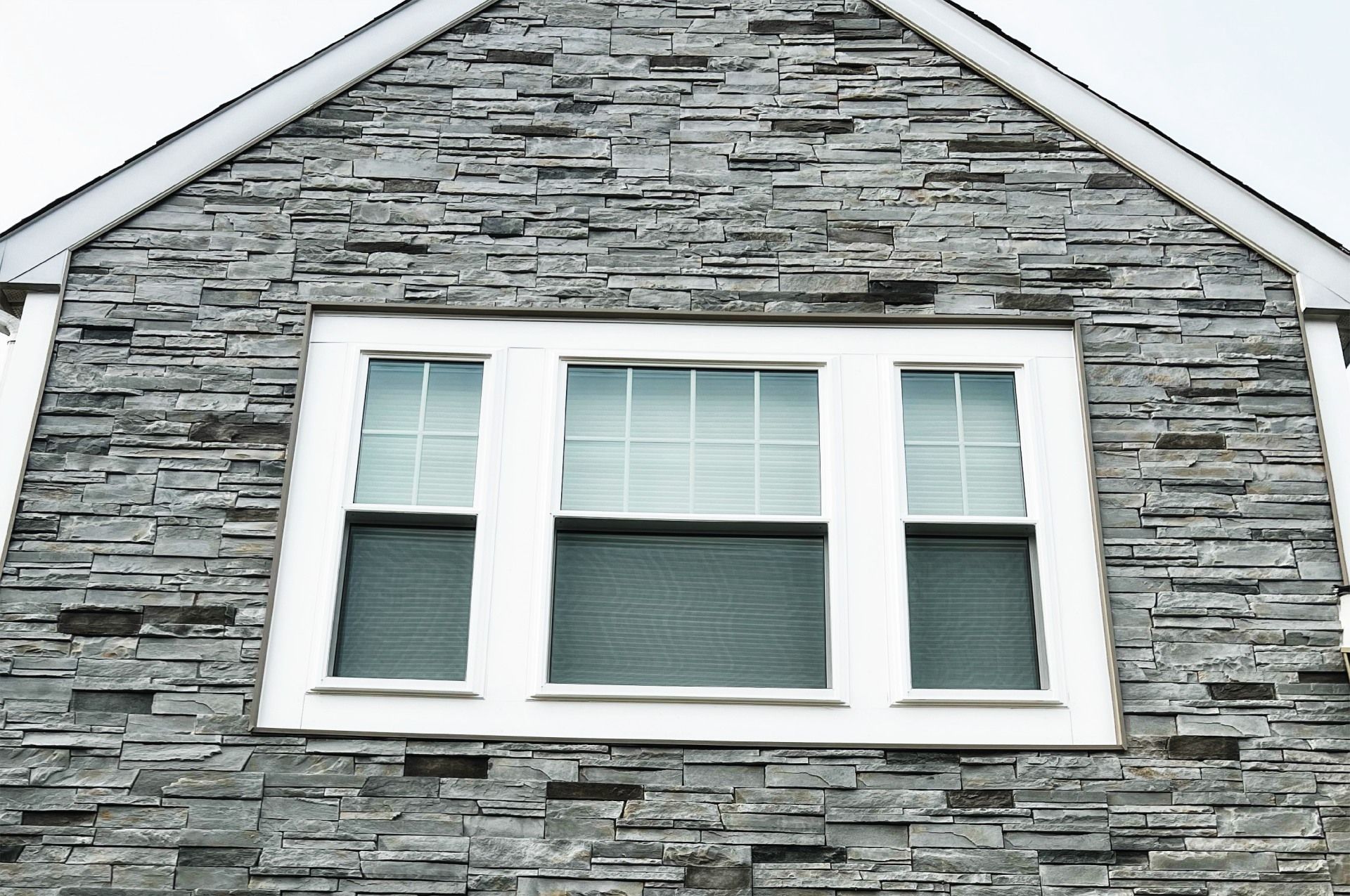 Grey stone facade with white-framed triple window; blinds visible.