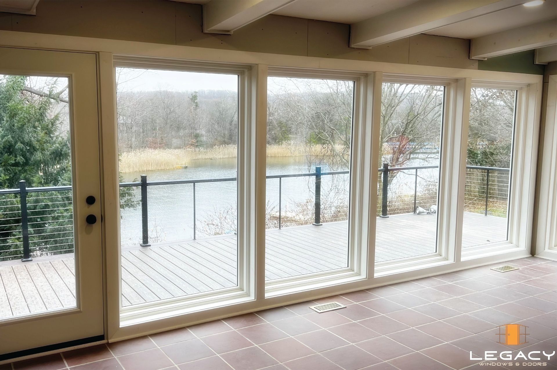 Large windows and door overlooking a deck and water. White frames and a dark railing are visible.