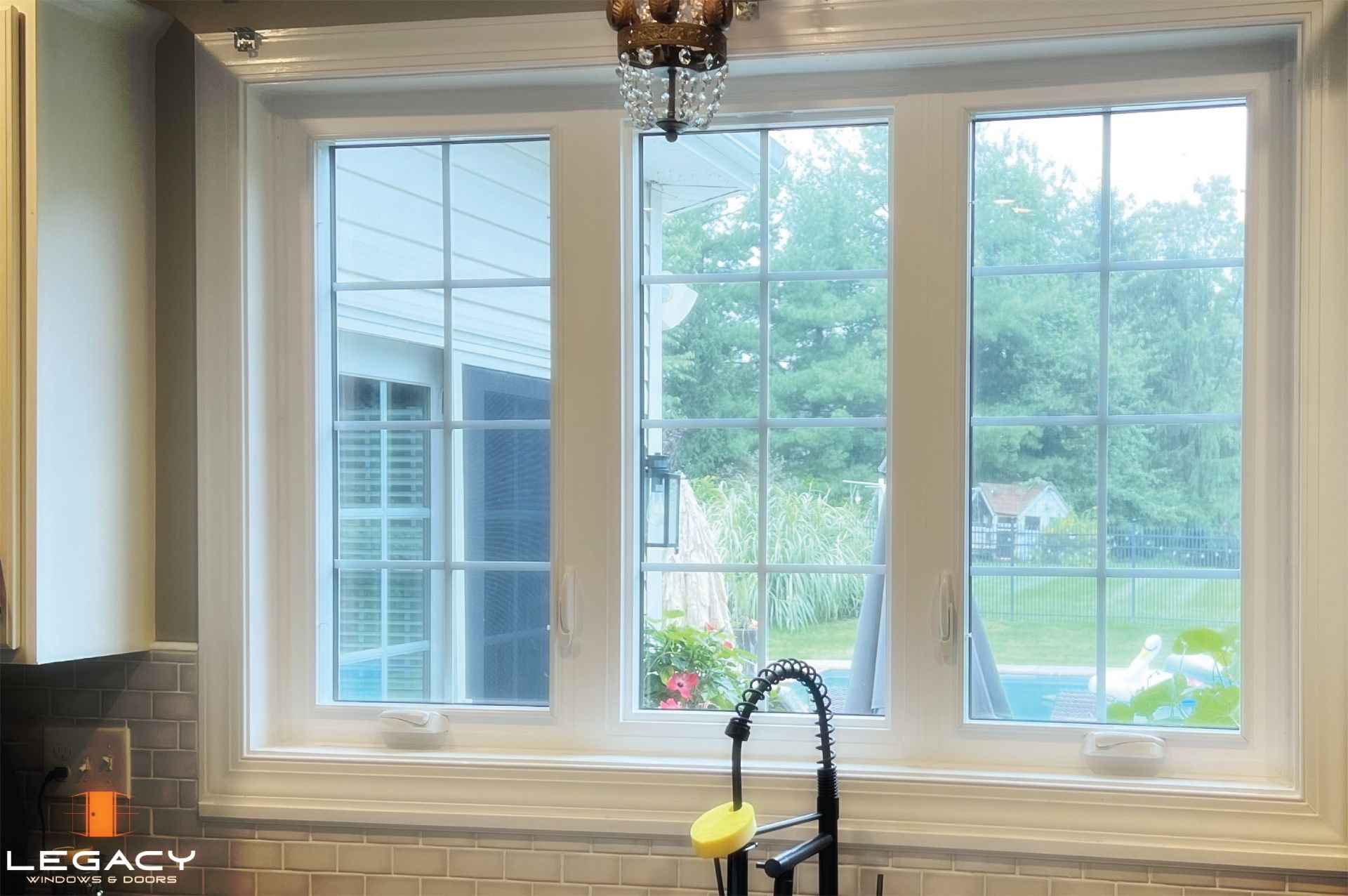Kitchen window with white frame and grids, overlooking a backyard with trees and a house.