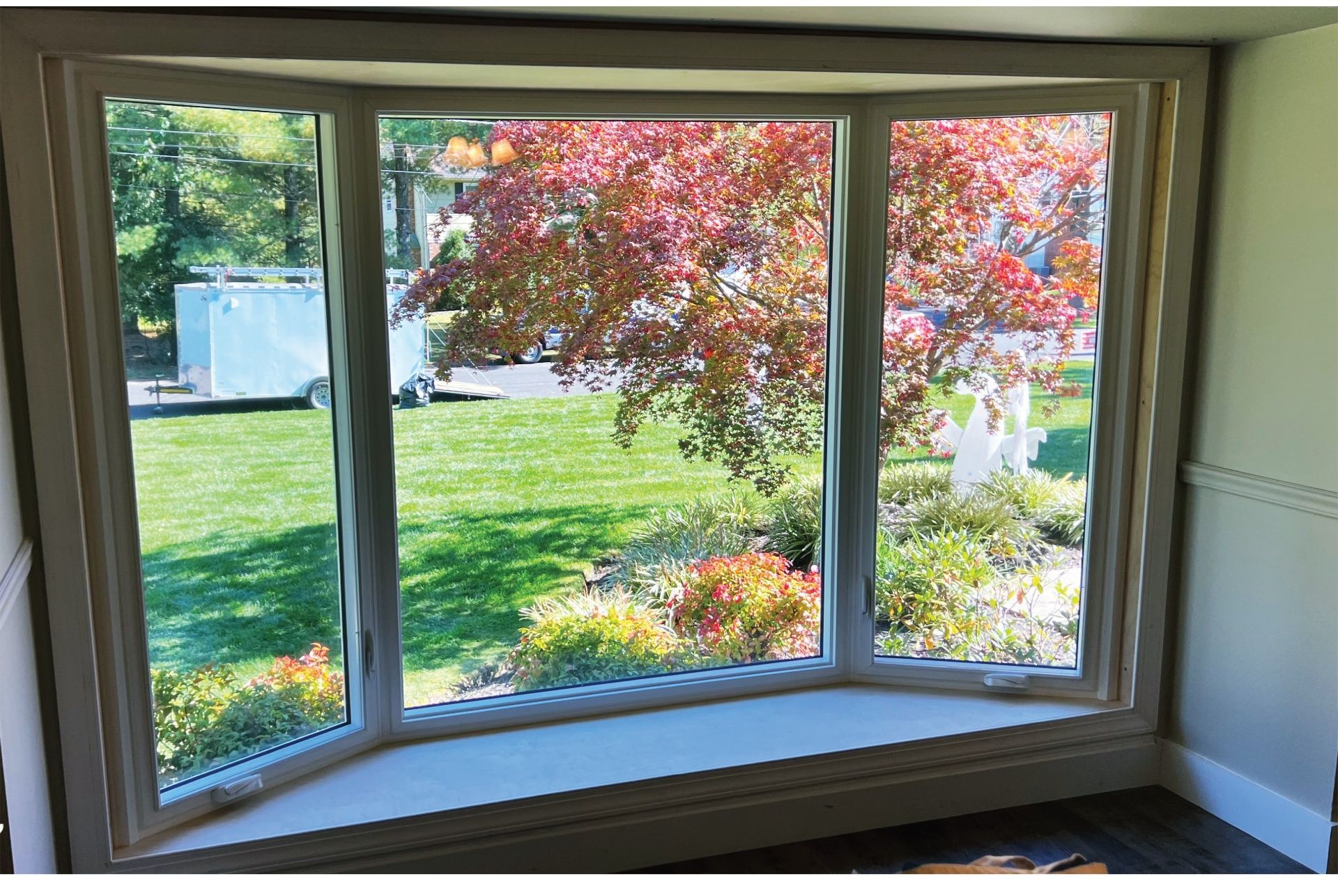 Bay window with a view of a yard and colorful tree. White frame, grass, blue sky.