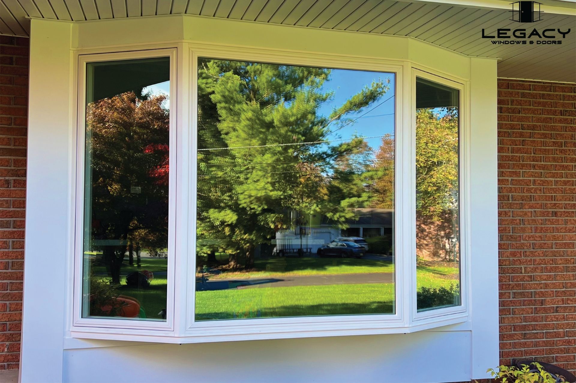 Bay window with white trim reflecting trees and a house on a brick exterior.