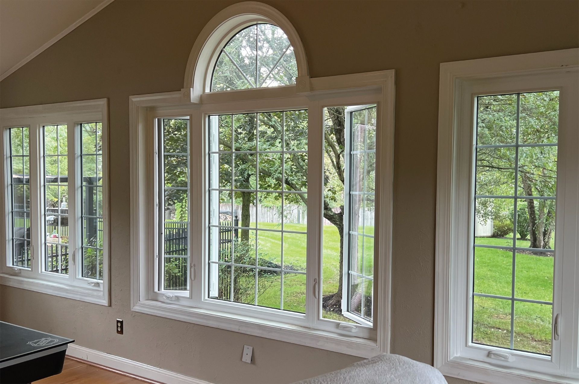 White-framed windows with grids and arched top, looking out at a green yard. Beige interior walls.