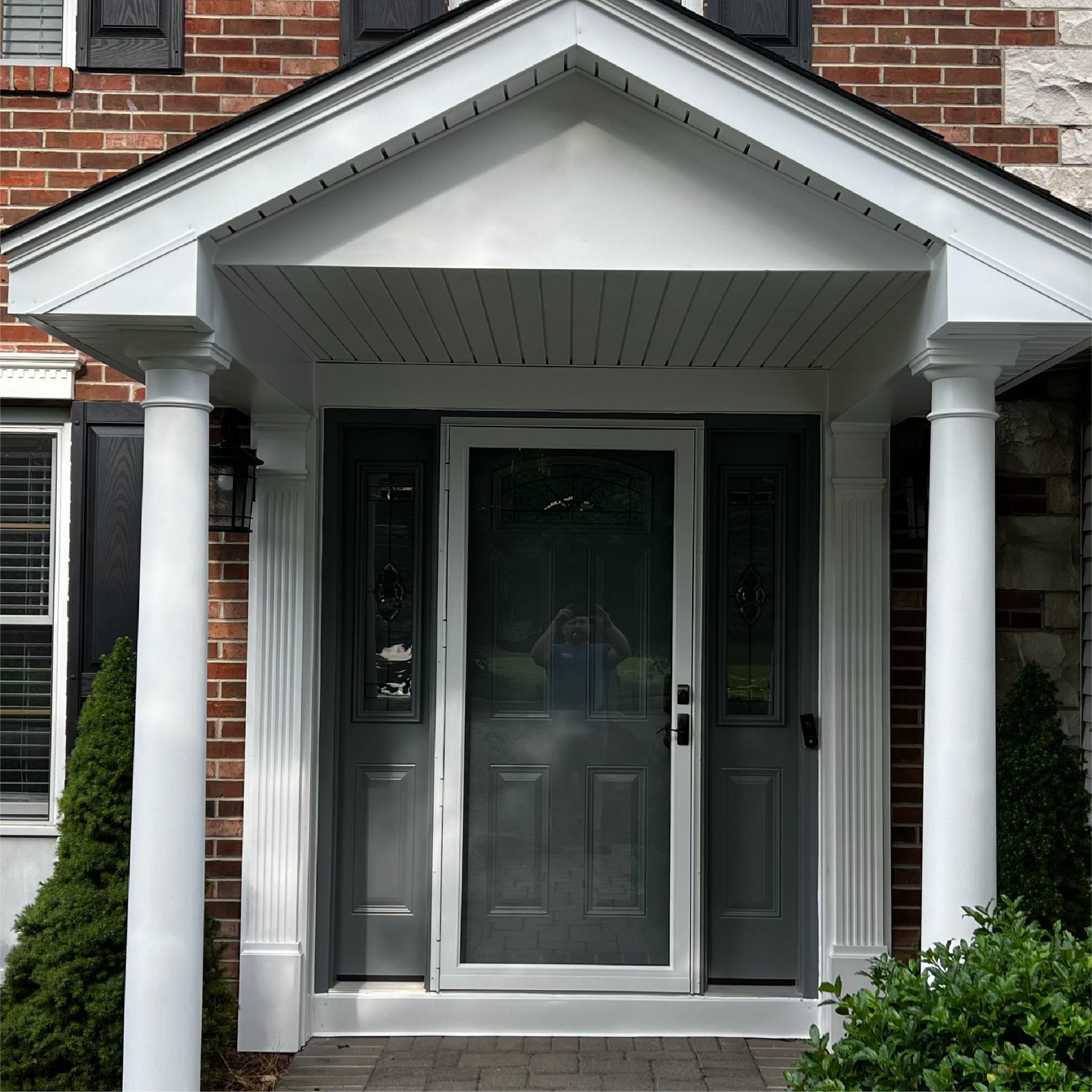 White-columned covered front door entry of a brick house with dark gray door and sidelights.