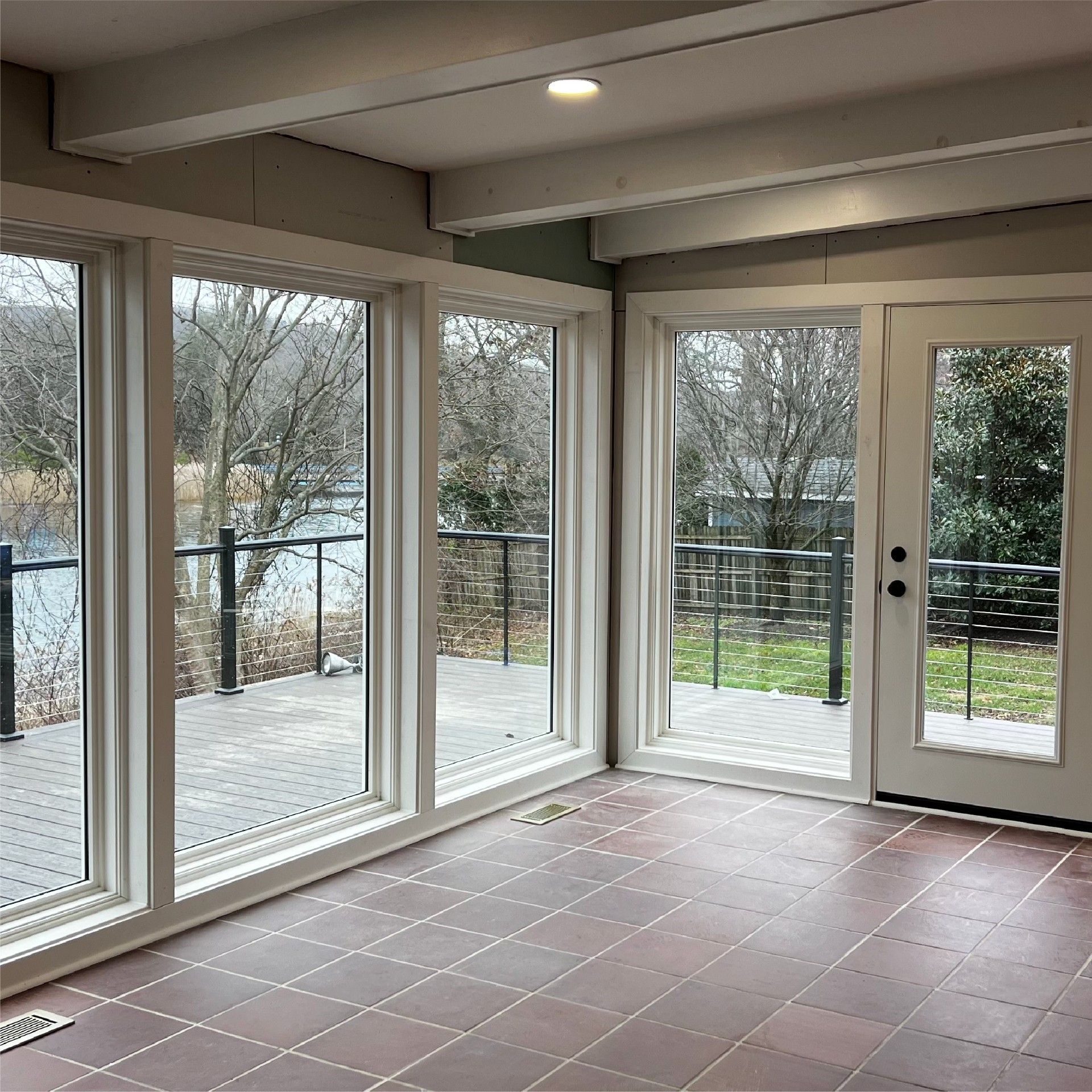 Sunroom with large windows, brick floor, overlooking a deck and river.