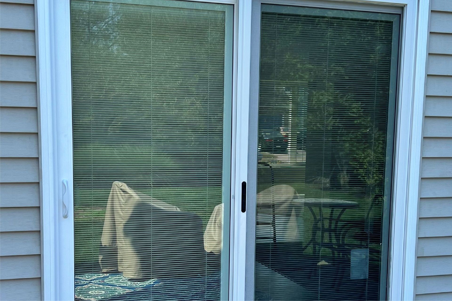 Sliding glass door with blinds closed, reflecting the outdoor patio and lawn.