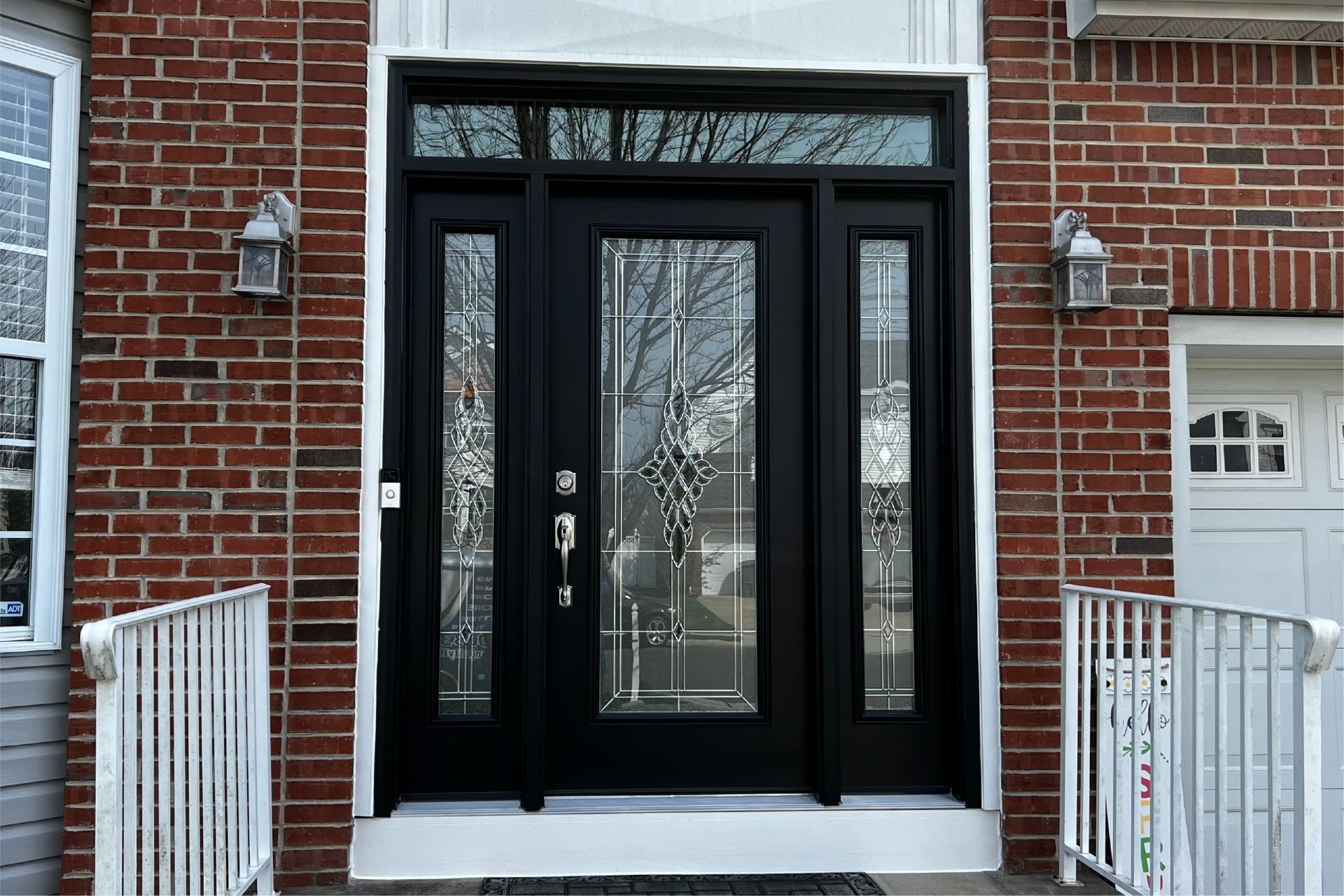 Black front door with glass panels on a brick house. White trim and railings.