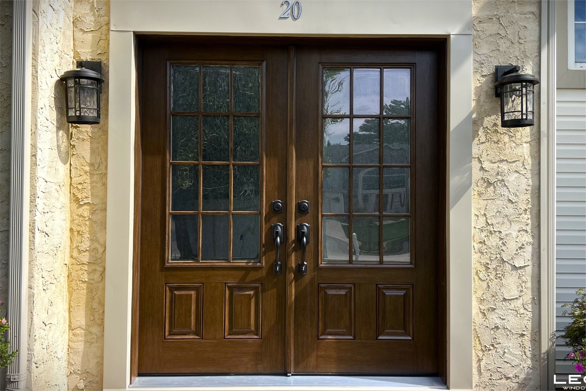 Brown double doors with glass panels and sidelights on a stucco building with address number 20.
