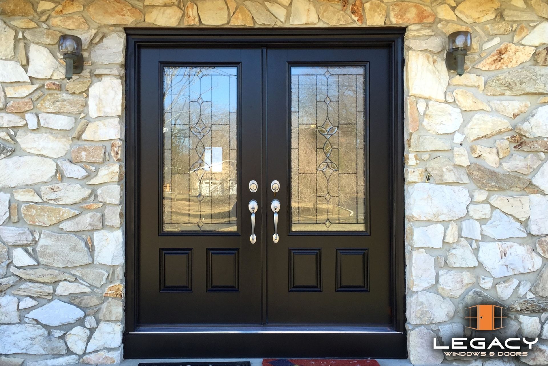 Black double front doors with decorative glass panels set in a stone wall.