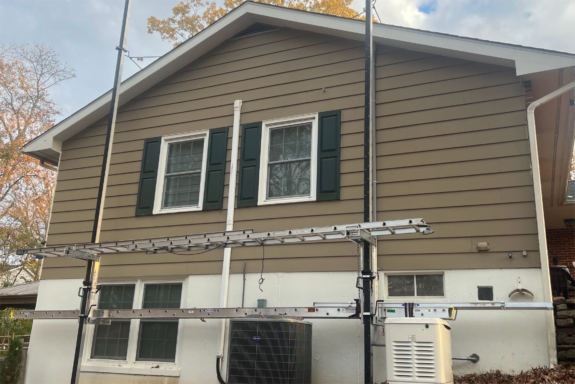 House with tan siding, green shutters, scaffolding set up on the side.