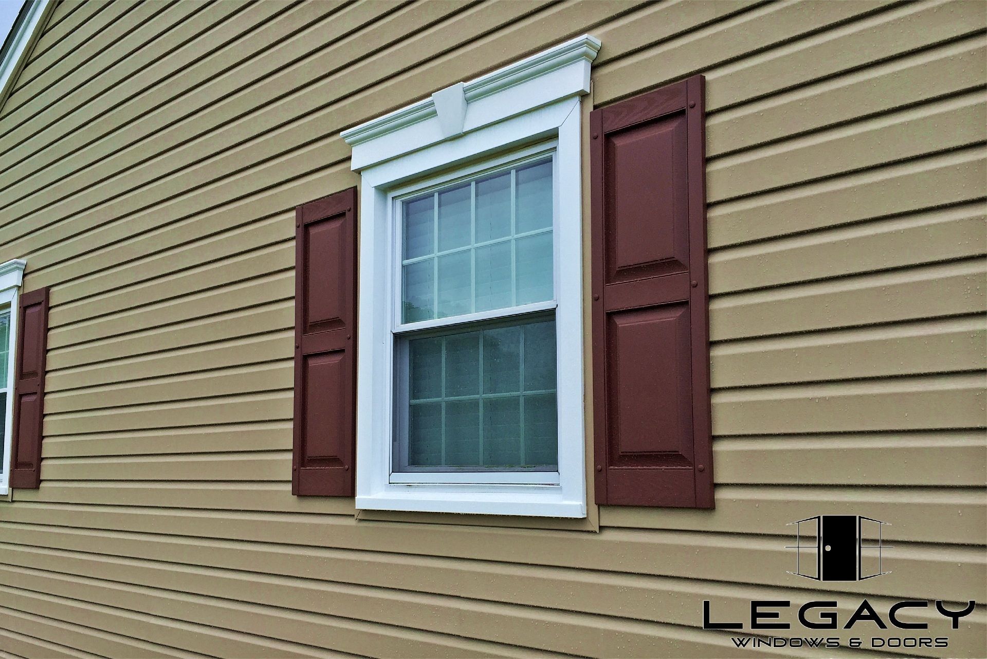 Tan siding with a window, white trim, and maroon shutters.