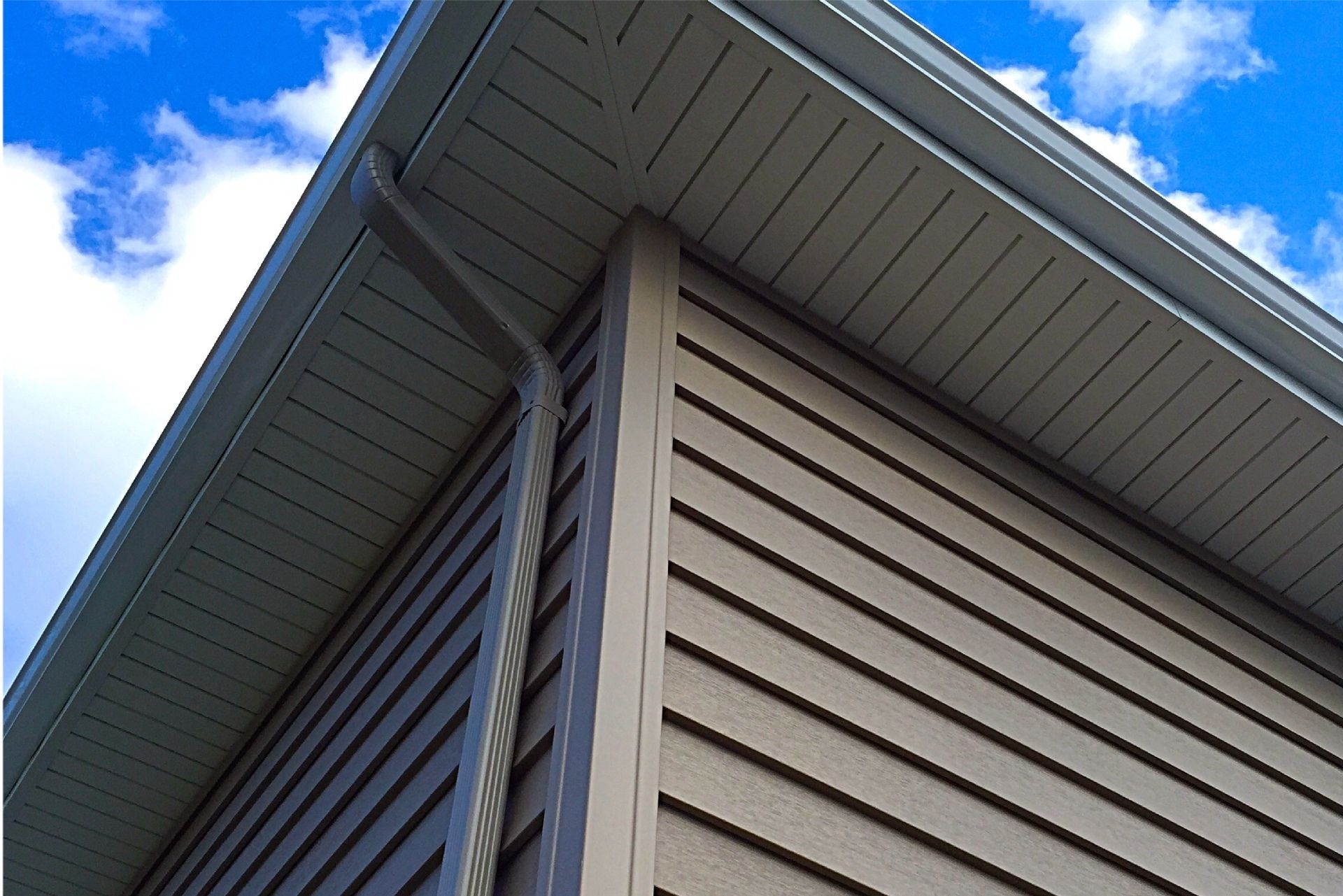 Corner of a building with light brown siding, gray soffit, and blue sky.