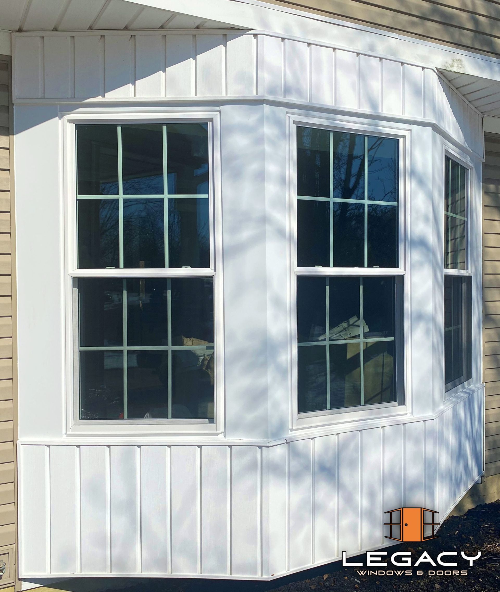 White bay window with vertical siding, featuring three paneled windows with grids.