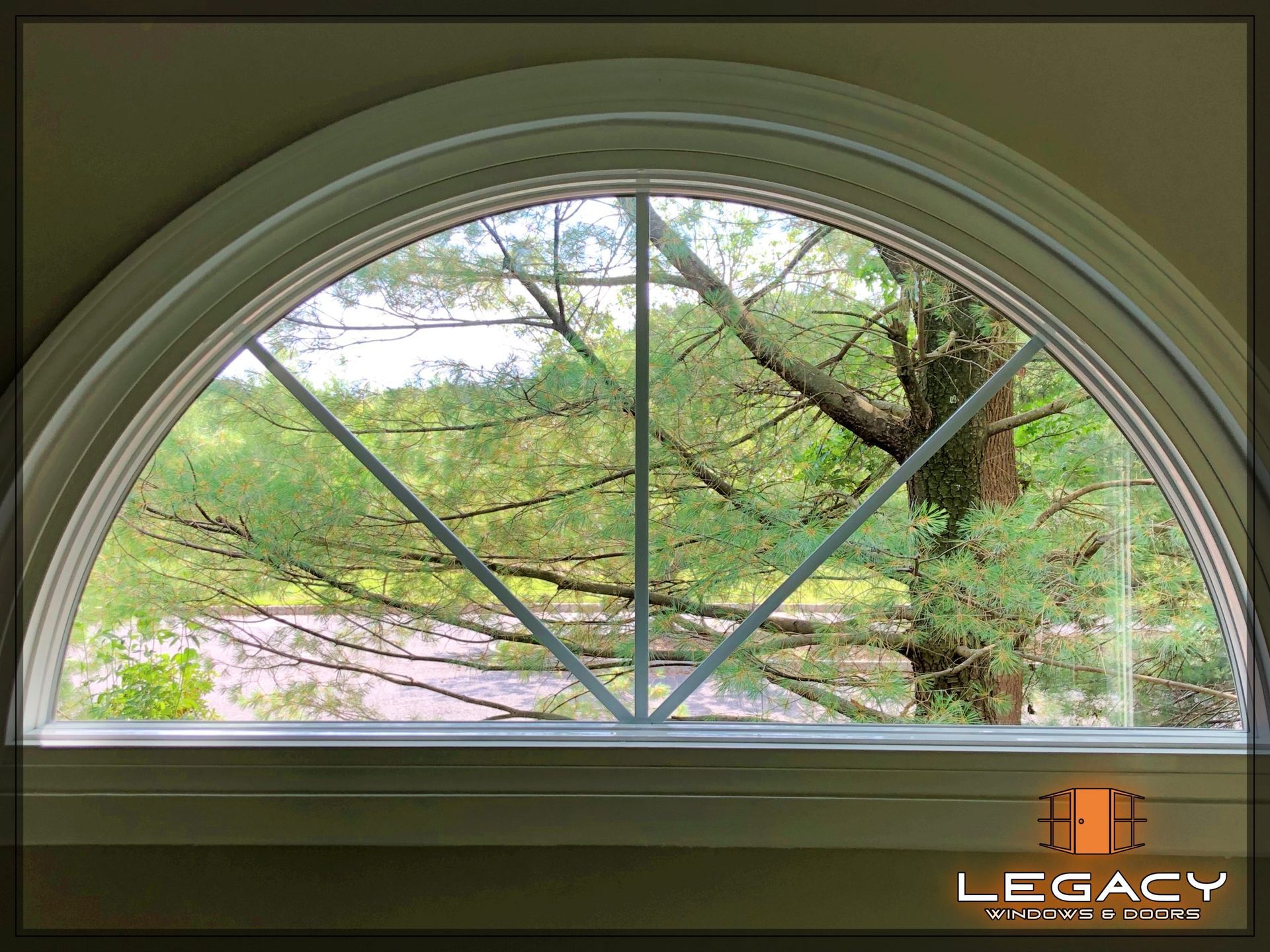 Arched window with white trim and a cross-shaped grid, framed view of trees and foliage.