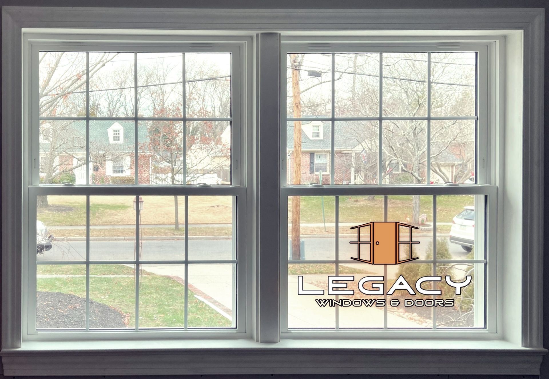 Two white, paneled double-hung windows with grid patterns overlooking a residential street.