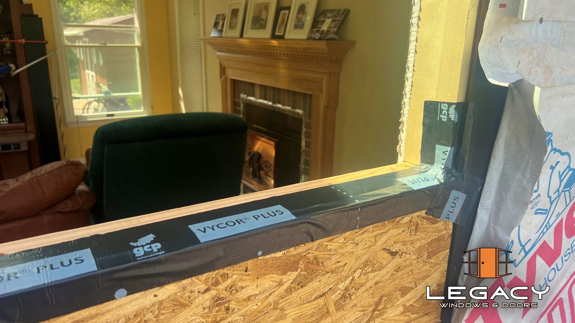 View through a window frame to a room with a fireplace and furniture. Construction in progress.