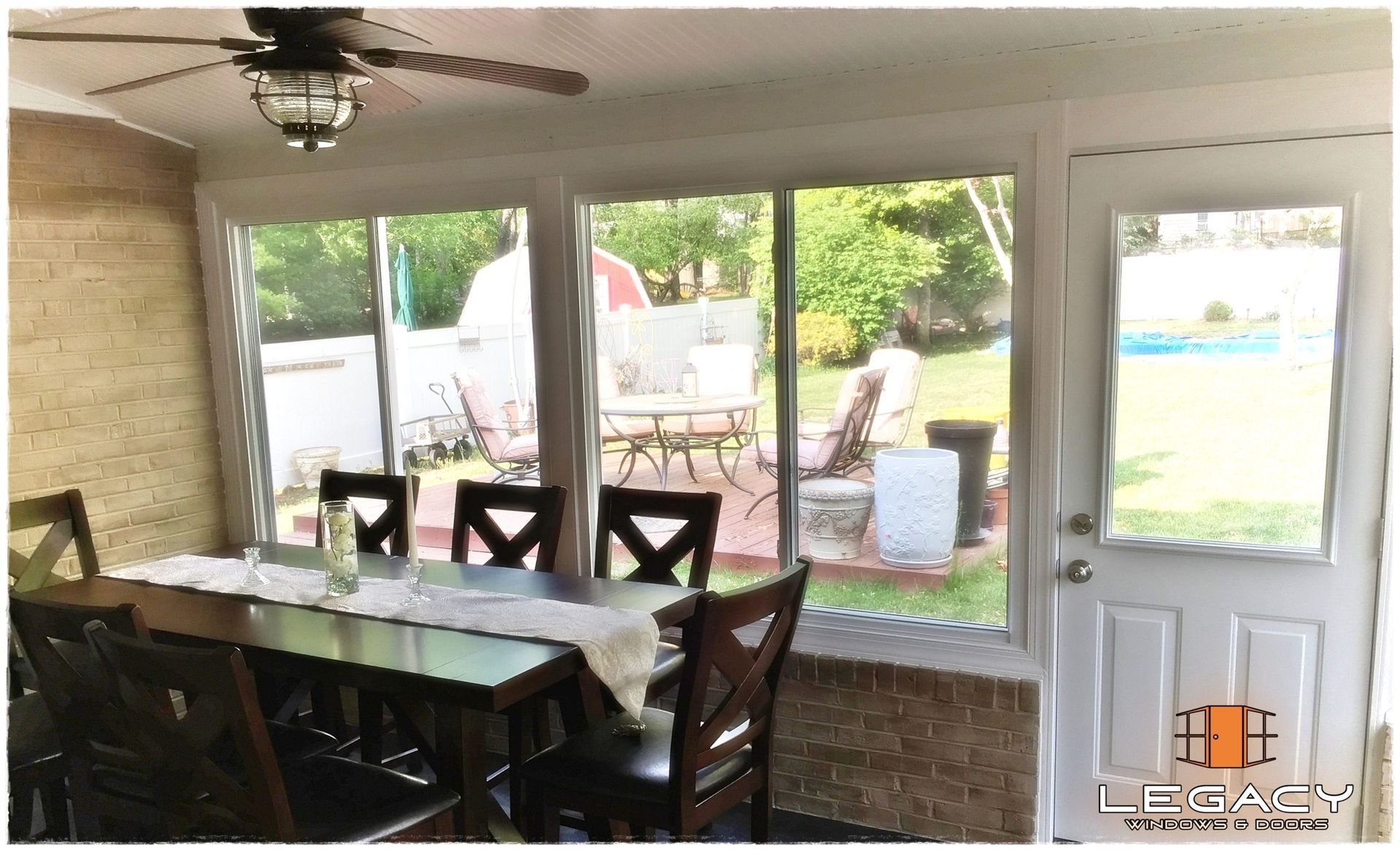 Sunroom interior with a dining table, chairs, large windows overlooking a backyard patio.