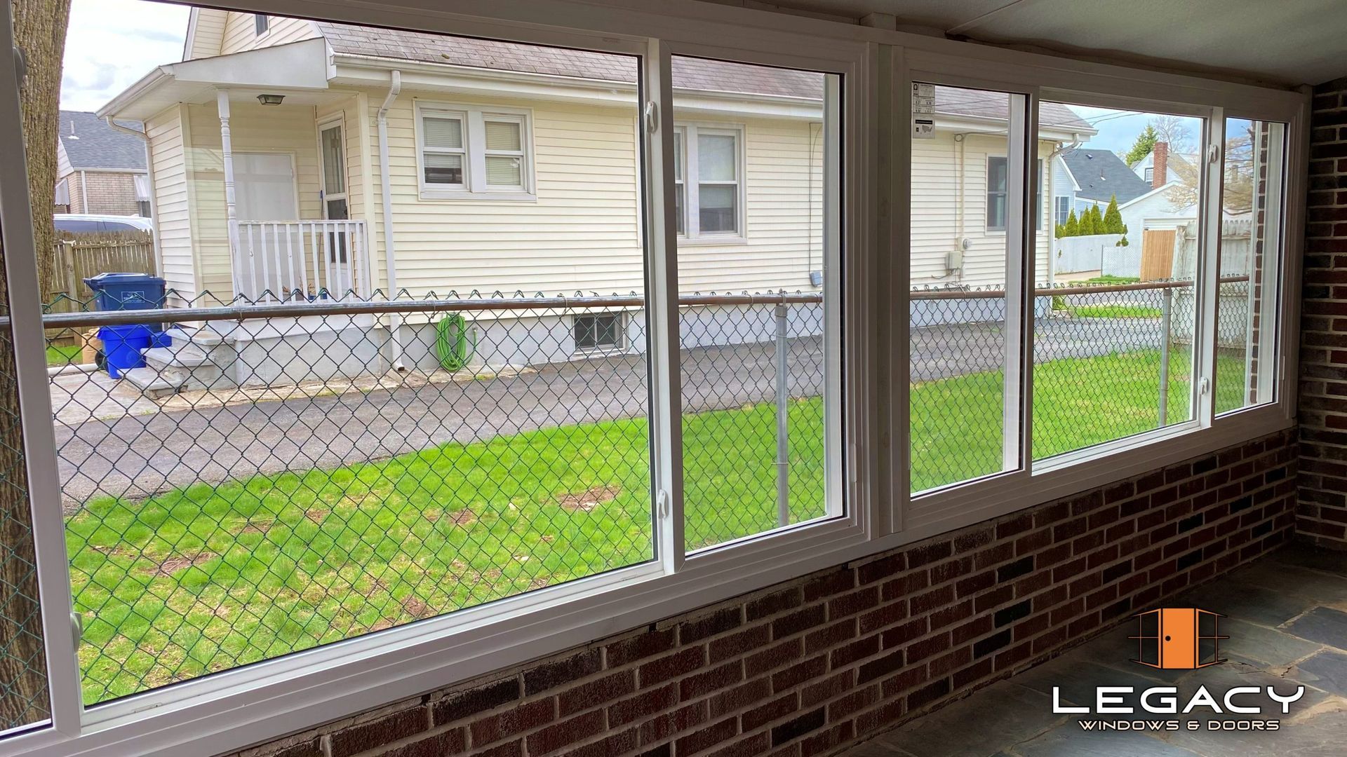 Sunroom with white-framed windows, brick wall, and view of a yard and house.
