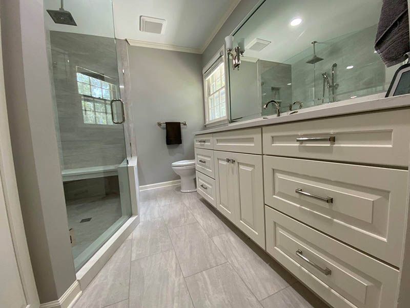 A bathroom with white cabinets , a toilet , and a walk in shower.