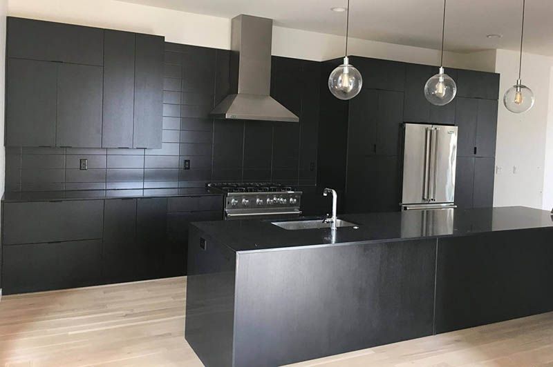 A kitchen with black cabinets and a large island in the middle.