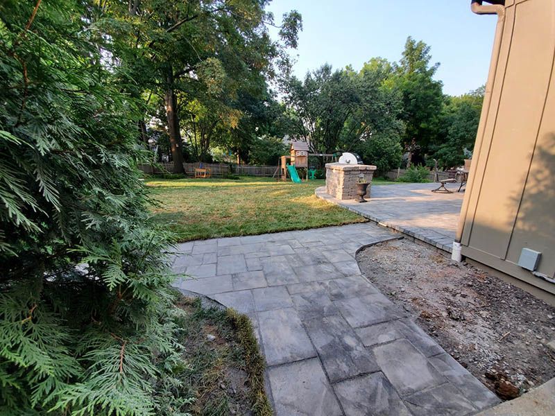 A stone walkway leading to a backyard with a playground in the background.