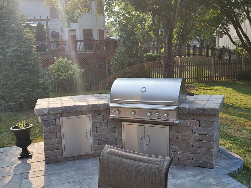 A grill is sitting on top of a brick counter in a backyard.