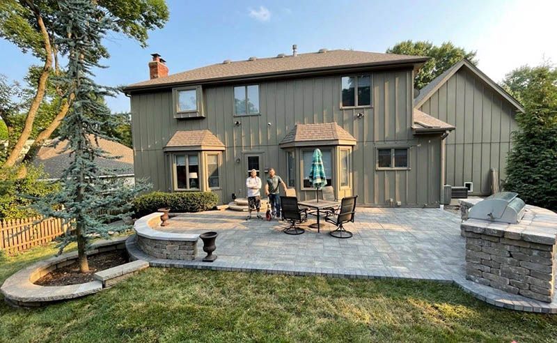 A couple of people standing on a patio in front of a large house.