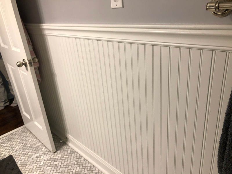 A bathroom with white wainscoting and a door.