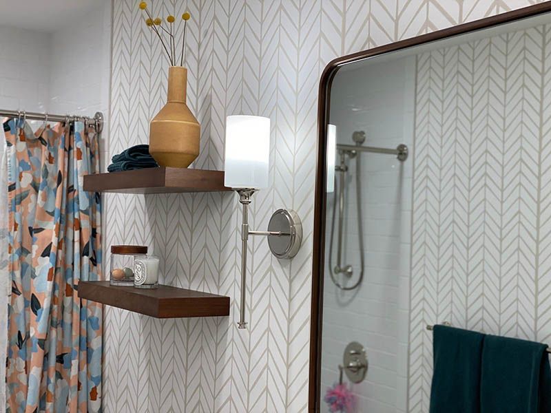 A bathroom with a shower , mirror , shelves and a vase on the wall.