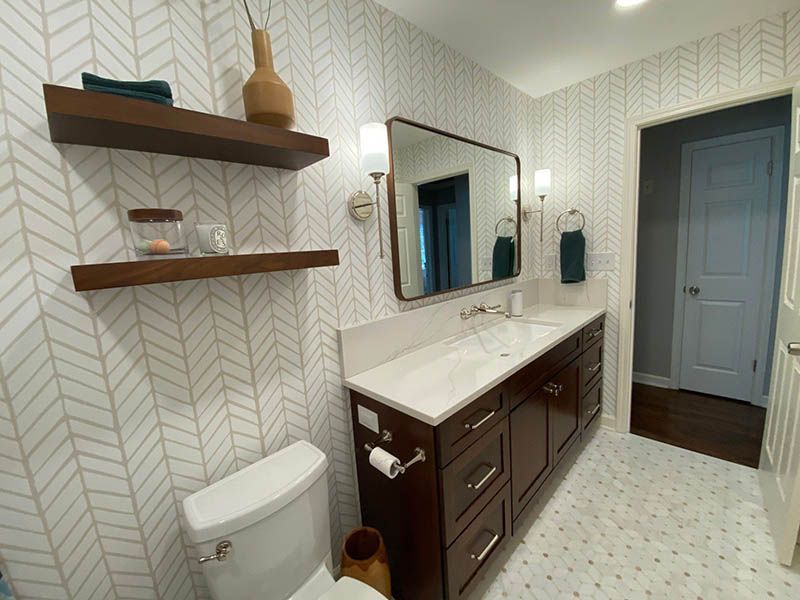 A bathroom with a toilet , sink , mirror and shelves.